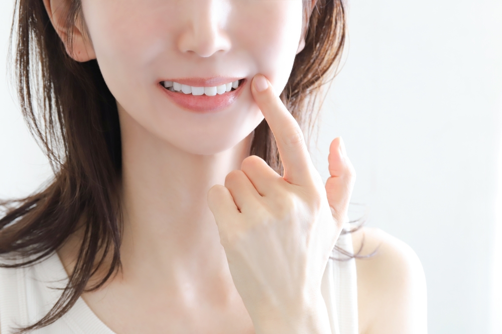 白い歯を指さして笑う女性